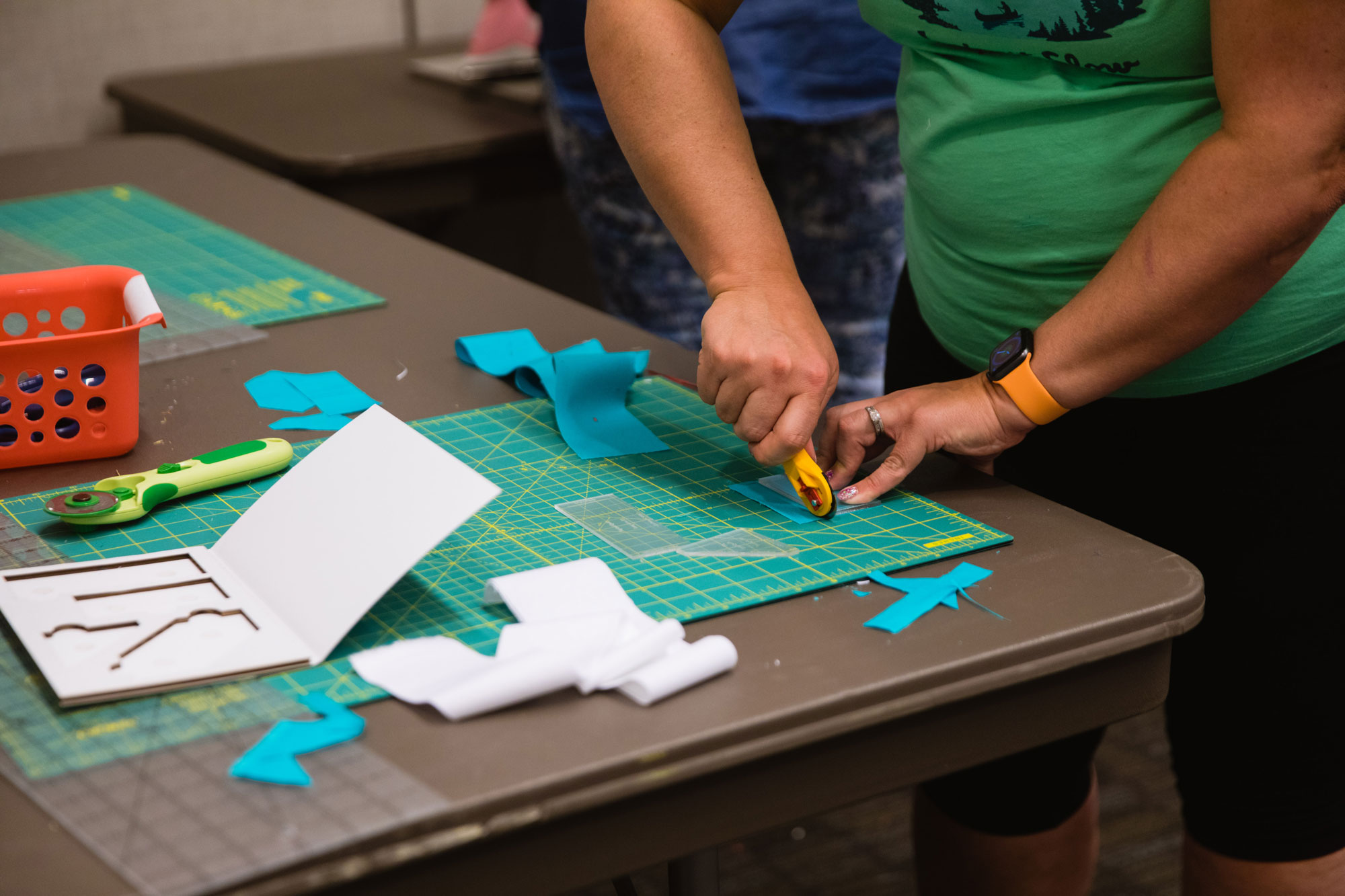 a person in a green shirt using a rotary cutter on fabric.